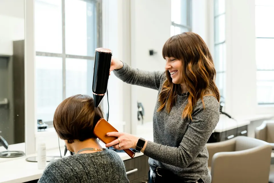 Cabeleireira finalizando o cabelo de uma cliente no salão